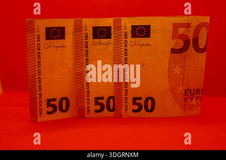 Three 50 Euro banknotes lie side by side on a striking red surface, revealing their intricate patterns and colors. The banknotes catch the light, addi Stock Photo