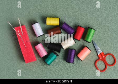Spools of thread, scissors and needle on green background Stock Photo
