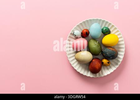 A collection of vibrant Easter eggs in various colors is artfully arranged on a white plate, set against a soft pink background, capturing the essence Stock Photo