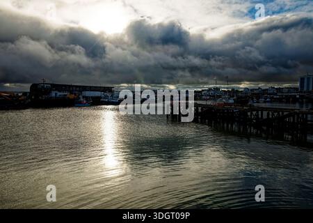 Late afternoon Sun breaks through rain clouds and shines across the water of Bridlington Harbour, East Yorkshire, England. Stock Photo