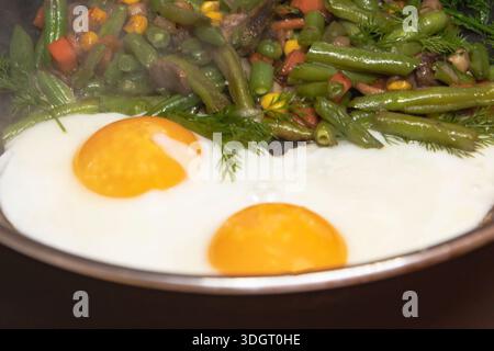 Fried eggs with mixed vegetables green beans mushrooms and herbs cooking in frying pan Stock Photo