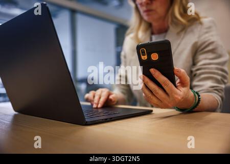 Businesswoman using laptop and smartphone during workday in office. Multitasking, online communication and digital business concept Stock Photo