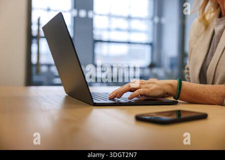 Woman manager typing on laptop at office desk, smart phone within reach. Workplace at corporate business office Stock Photo