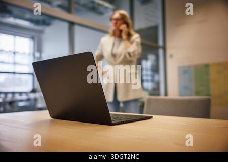 Leader manager woman standing in office desk with laptop, talking to smartphone. Leadership, corporate communication and modern workplace concept Stock Photo