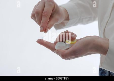 Close-up hands holding contact lens on fingertip with storage case on white background, ideal for optometry website banner or education about lens hyg Stock Photo
