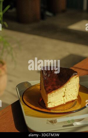 Slice of classic baked cheesecake on a ceramic plate, creamy interior with a golden brown top, warm natural light creating a cozy and minimalist desse Stock Photo
