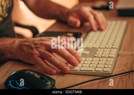 Close-up of male hands typing on computer keyboard with mouse and smartphone, selective focus Stock Photo