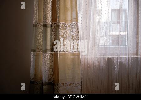 Soft sheer curtain fabric with delicate patterns, filtered natural light, and gentle shadows creating a calm and warm interior texture background. Stock Photo