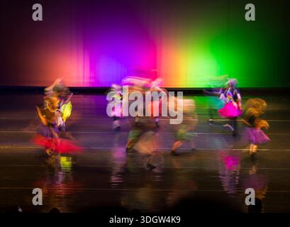 Dancers moving in colorful costumes on a stage reflecting vibrant rainbow lights Stock Photo