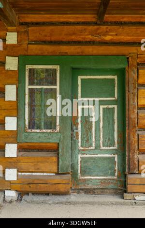 Weathered green door and white framed window on a rustic wooden folk house in Osturna, Slovakia Stock Photo