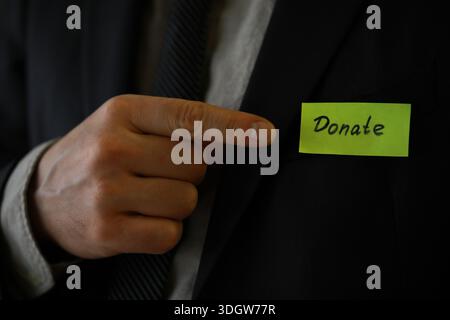 Businessman shows a wooden block with the word donate. Charitable donation in business concept. Stock Photo