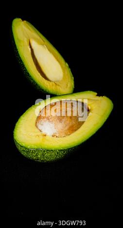 Two halves of fresh ripe avocado with seed showing creamy texture on dark moody background. Stock Photo