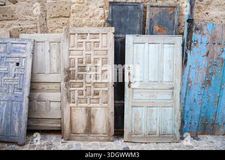 Weathered antique wooden doors with peeling paint and patterns leaning against stone wall, showing rustic texture Stock Photo
