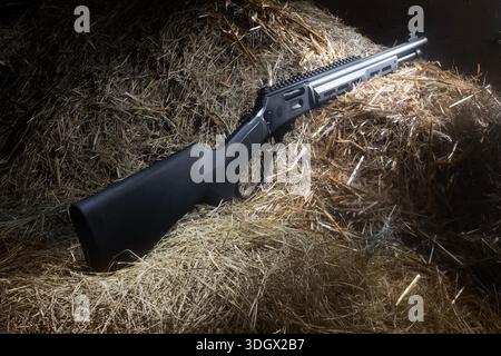 Modern black lever action rifle with a rail for mounting a scope on hay in a dark barn. Stock Photo