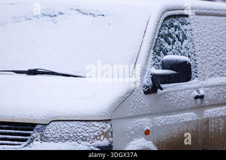 Snow-covered parked car in winter. Front view of parked car covered with fresh snow, winter urban lifestyle and cold weather conditions. Stock Photo