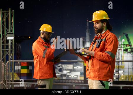 Offshore sea platform professionals using laptop to analyze extraction efficiency during 24 hour operation. Drilling rig technicians configuring vessel management systems, working late at night Stock Photo