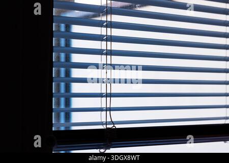 Close up of horizontal window blinds with a hanging cord and soft daylight and shadow Stock Photo