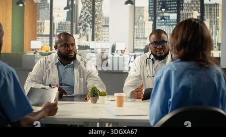 Group of specialists and medics collaborating in a hospital conference room. Healthcare staff brainstorms treatment ideas and wellness advancements through teamwork and communication. Stock Photo