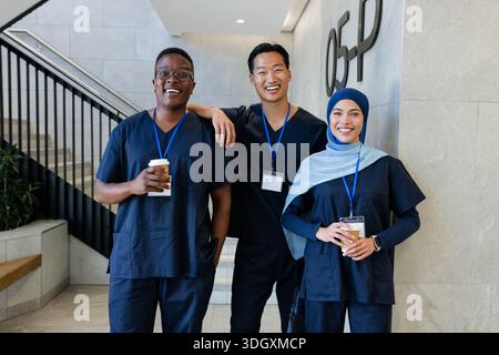 Diverse medical staff wearing navy scrubs standing in hospital lobby holding cups and blue IDs Stock Photo