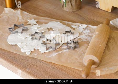 Festive Christmas baking process with rolled dough, metal cookie cutters for gingerbread and wooden rolling pin on parchment paper. Holiday kitchen sc Stock Photo