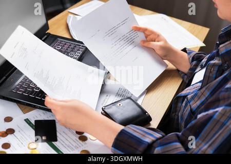 A top-down view of a woman at a desk, holding financial documents, reviewing numerous bills and financial records. Concept for home accounting, auditi Stock Photo