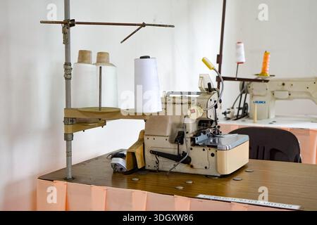 Johor, Malaysia, September 9, 2025: Close-up of industrial sewing machine with multiple thread spools and lighting in a textile production workspace. Stock Photo