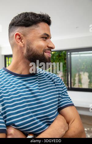 Man standing in modern home, facing right, wearing blue-white striped tee, showing wristwatch Stock Photo
