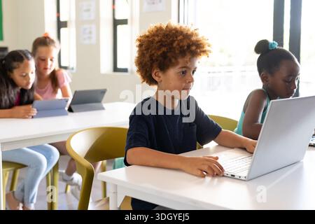 School child boy sitting at desk wearing dark navy T-shirt using silver laptop in classroom Stock Photo