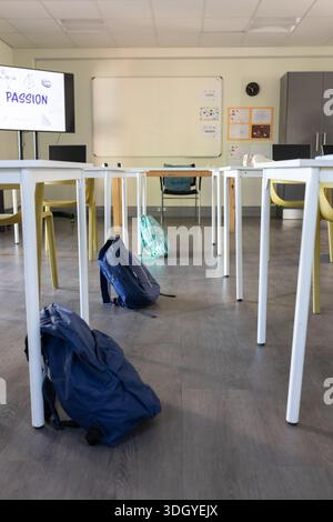 Navy backpack is sitting on aisle between white tables and yellow chairs, PASSION display at front Stock Photo