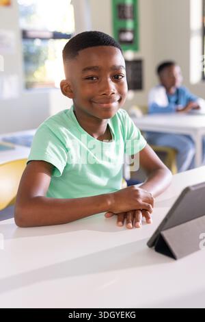 African American child sitting in classroom at desk wearing mint t-shirt using tablet in folio case Stock Photo