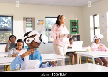 African American male child reaching forward wearing white VR headset and blue shirt in classroom Stock Photo