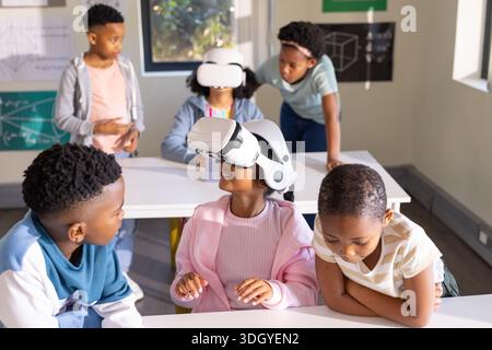 African American students wearing white VR headsets and interacting at classroom desks with posters Stock Photo