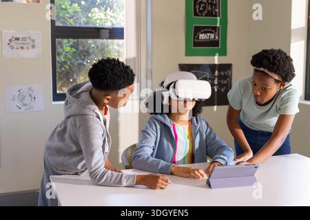 African American teens in class using VR headset, center girl wearing hoodie, using tablet Stock Photo