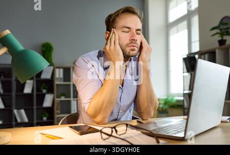 Headache and stress of workaholic man working late with laptop in office Stock Photo
