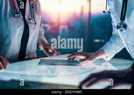 Two medical professionals interacting with touch screen in a futuristic setting, analyzing data and collaborating on innovative healthcare solutions Stock Photo