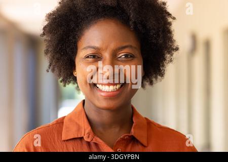 Adult woman smiling in building corridor, wearing rust collared shirt and stud earrings Stock Photo