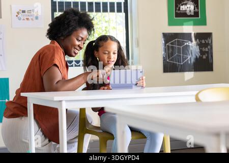African American female teacher and youth female student using tablet in classroom with posters Stock Photo