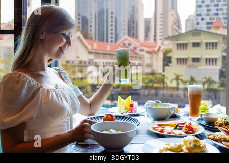 Woman enjoying lunch in city restaurant, holding green smoothie, with Stock Photo