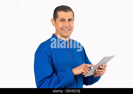 Confident smiling professional handyman in blue overalls using digital tablet with white background. Stock Photo