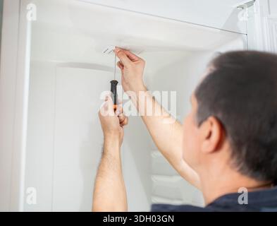 Male repairman fixing refrigerator with screwdriver at house Stock Photo