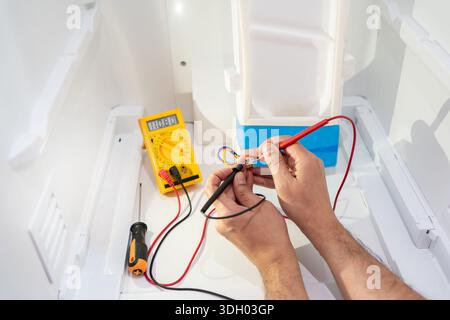 Close-up of an electrician repairing a refrigerator power outlet and measuring the voltage with his multimeter Stock Photo