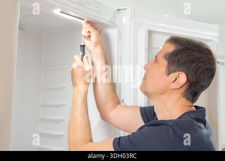 Male repairman fixing refrigerator with screwdriver at home Stock Photo