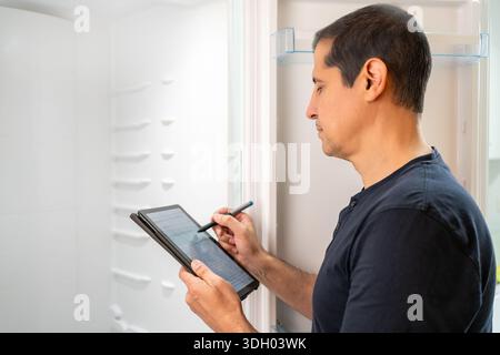 Male technician checking refrigerator and noting the data on the tablet Stock Photo