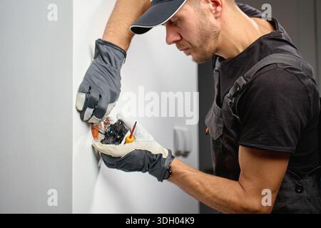 Electrician installing electrical wall switch and connecting wires inside wall using screwdriver. Concept of professional electrical work, home renovation and safe installation. Stock Photo