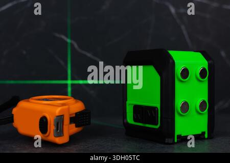 Construction tools, green laser level measurer and tape measure on dark background. Stock Photo