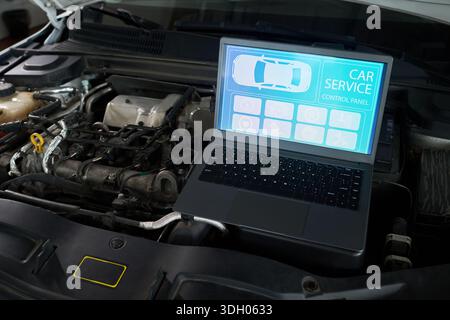 Laptop displaying car service control panel screen placed on open engine compartment, showing diagnostic interface for vehicle maintenance and repair in automotive workshop setting Stock Photo