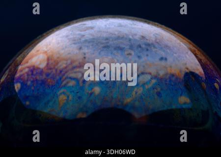 Close-up of a colorful soap bubble showing vibrant swirling patterns on a dark background, perfect for abstract and creative designs. Stock Photo