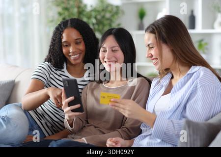 Three happy diverse friends buying online using credit card and smart phone at home Stock Photo