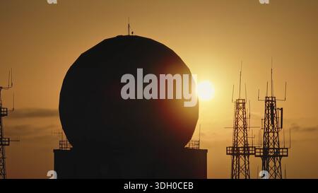 Telecommunication towers and a radar dome are silhouetted against the ...