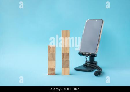 Square wooden blocks stacked in two sets next to smartphone. On light blue background. Stock Photo